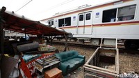 Commuter line melintas di rel yang pingginya dipenuhi bangunan liar.