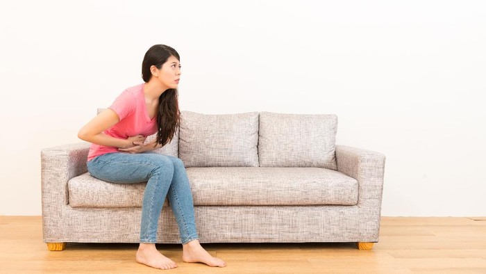 young woman sitting on sofa making pain gesture