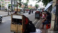 Para pedagang menunggu pembeli sambil duduk-duduk di atas trotoar.