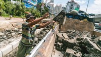Seorang pekerja membersihkan area proyek dari pecahan aspal dengan ditampung ke mobil bak.