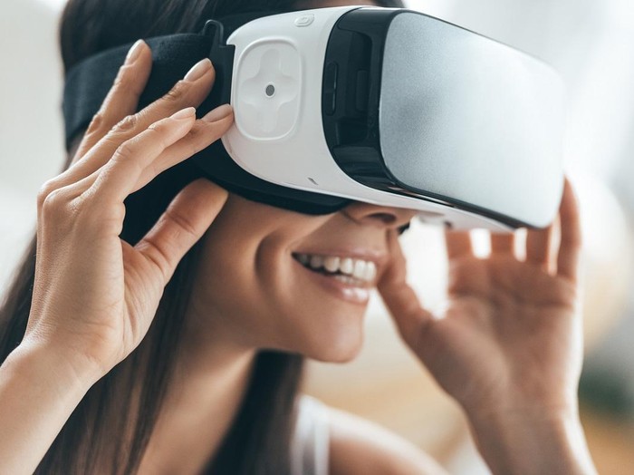 Attractive young woman adjusting her VR headset and smiling while sitting at home