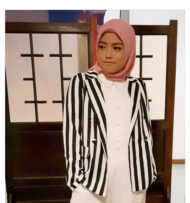 Tika Ramlan bergaya monokrom dengan padu padan kemeja putih dan striped blazer. Garis vertikal pada blazer penyanyi berdarah Bandung itu mampu memberikan ilusi tubuh ramping. Penampilan terlihat cerah dengan pemakaian kerudung merah muda. Foto: Dok. Instagram @tika_ramlan
