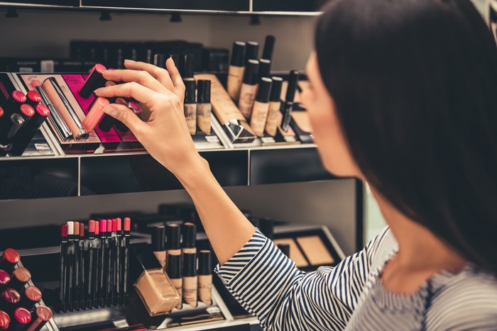 662134022 Beautiful girl is choosing lipstick while doing shopping in the mall