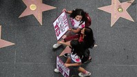Para perempuan ikut membawa tulisan sambil berjalan melintasi Walk of Fame.
