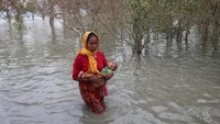 Sambil menggendong bayi, seorang wanita pengungsi Rohingya menyeberangi sungai. Mohammad Ponir Hossain/Reuters.