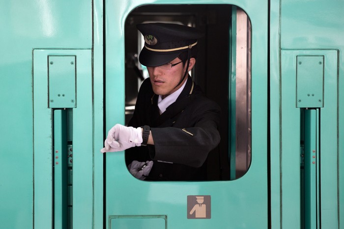 TOKYO, JAPAN - MAY 02:  A train guard checks his watch ahead of departure as he leans out of a window on a Shinkansen bullet train at Tokyo Train Station on May 02, 2016 in Tokyo, Japan. The Shinkansen is a network of high-speed railway lines in Japan currently consisting of 2,764.6 km (1,717.8 mi) of lines with maximum speeds of 240-320 km/h (150-200 mph). The network presently links most major cities on the islands of Honshu and Kyushu, and Hakodate on northern island of Hokkaido. The maximum operating speed is 320 km/h (200 mph) though test runs have reached up to a world record 603 km/h (375 mph) for maglev trains in April 2015.  (Photo by Carl Court/Getty Images)