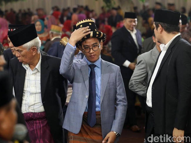 Di saat para tetua terlihat memakai setelan jas hitam dengan kemeja putih yang kancing atasnya dibiarkan terbuka, Gibran memilih sesuatu yang berbeda. Gaya andalan anti-mainstream Gibran terdiri dari kemeja biru berdasi senada yang dibalut jas abu-abu bermotif kotak. Celana bahan biru setumit menjadi pilihan suami Selvi Ananda itu untuk bawahan. Foto: Grandyos Zafna.