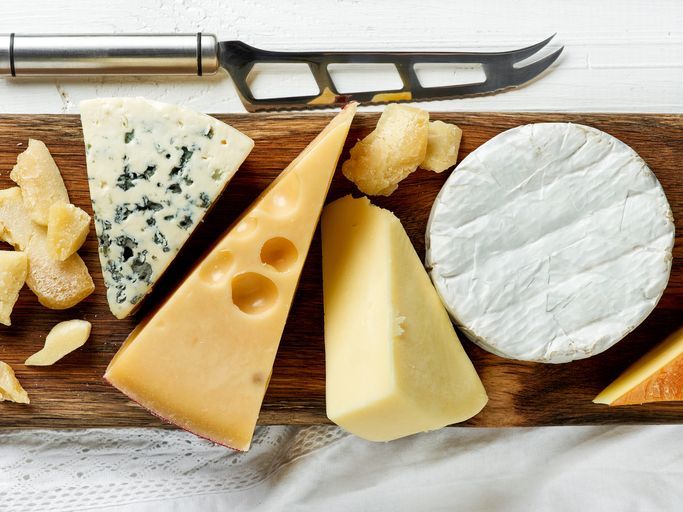 various types of cheese on rustic wooden cutting board, top view