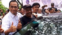 Budi Karya Sumadi berpose sambil mengacungkan jempol di samping taksi online yang telah dipasangi stiker.