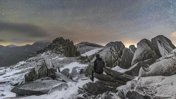 Seorang pengamat bintang duduk-duduk di salah satu puncak Castell-Y-Gwynt (Castle of the Winds) Gunung Glyder Fach di Snowdonia, Wales, di bawah langit malam dengan suhu yang membuat tubuh membeku. Foto: Kris Williams via PopSugar
