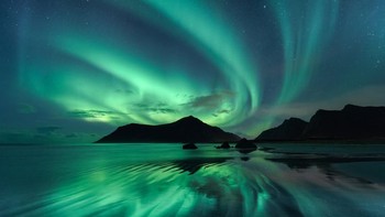 Refleksi di atas riak ombak pantai Skagsanden, Norwegia, mencerminkan pusaran hijau Aurora Borealis yang terlihat cemerlang di langit malam. Foto: Beate Behnke via PopSugar