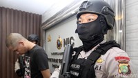 DR dihadirkan dalam jumpa pers dengan penjagaan polisi bersenjata api laras panjang.