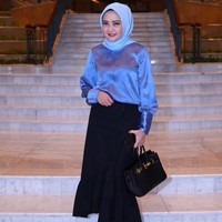 Gaya feminin Dewi Ramlan dalam balutan rok modifikasi warna hitam dan blouse biru satin. Gaya hijabnya tetap dibuat simpel hanya diikat ke belakang. Tas Hermes hitam memberikan kesan mewah dan elegan. Foto: Dok. Instagram @dewiramlan