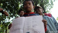 Fadil menunjukan raport hasil belajarnya di sekolah.
