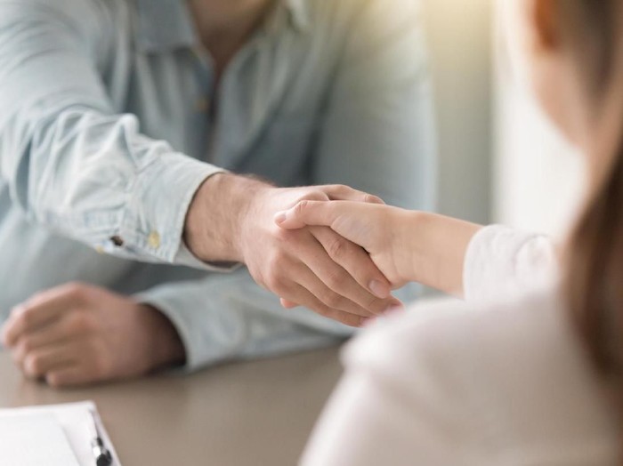 Businessman shaking female hand above the table. Business agreement and partnership concept. Partners closing a deal, view over the shoulder. Formal greeting gesture, effective negotiations