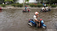 Para pengendara mendorong motornya yang mogok akibat menerobos banjir rob.