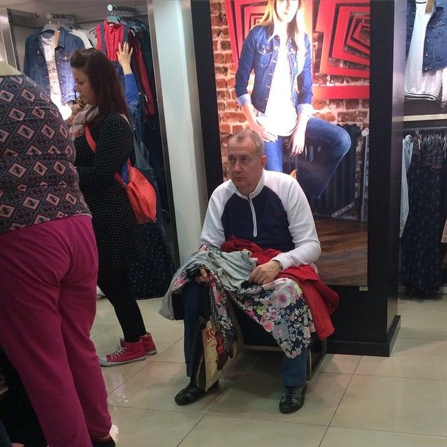 Studi yang diadakan Andrews Air Conditioning mengungkapkan, rata-rata pria menunggu 23 menit setiap sesi belanja, sambil berdiri atau duduk dengan canggung di depan toko atau kamar pas. Pria yang duduk sambil memegang baju-baju ini contohnya. Foto: Dok. Instagram Miserable Men