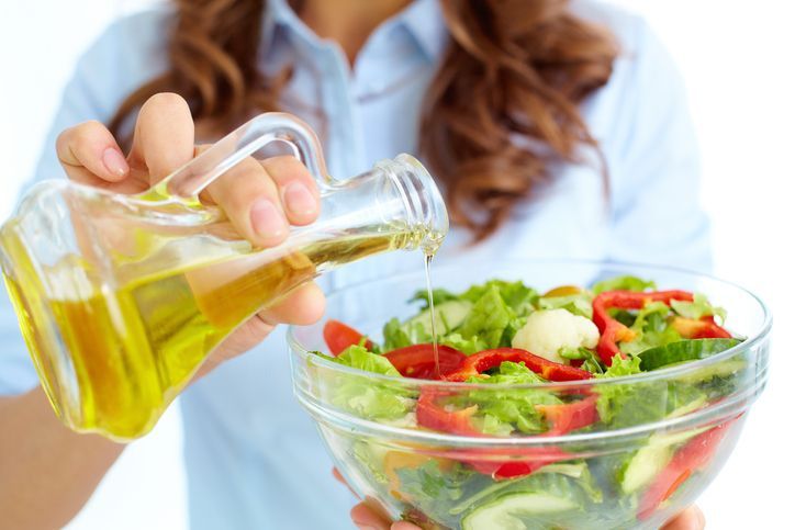 Close-up of female pouring oil into vegetable salad in glass bowl