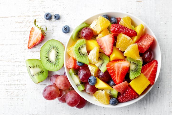 delicious fruit and berry summer salad decorated with mint leaves on clay dish on cutting board with dessert forks, half of peach and slice of melon on rustic boards, view from above