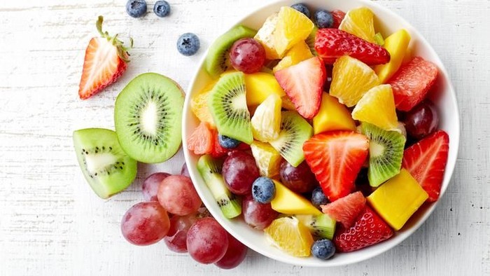 delicious fruit and berry summer salad decorated with mint leaves on clay dish on cutting board with dessert forks, half of peach and slice of melon on rustic boards, view from above