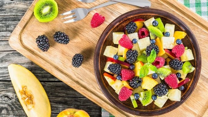 salad buah delicious fruit and berry summer salad decorated with mint leaves on clay dish on cutting board with dessert forks, half of peach and slice of melon on rustic boards, view from above