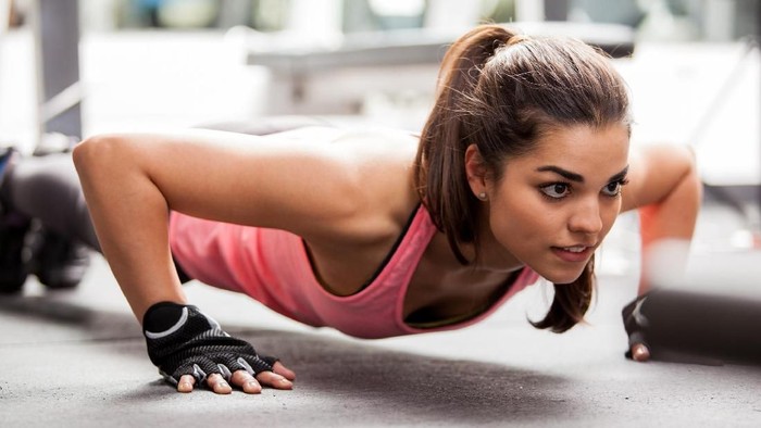Beautiful Latin woman doing push ups in the gym before lifting some weights