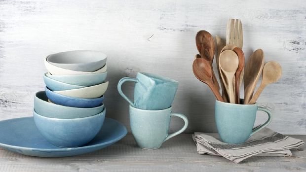 Simple rustic handmade blue crockery against white wooden wall: dish, stack of bowls. mugs and wooden cooking utensils set.