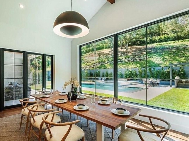 Di samping kolam renang, ada ruang berkaca yang digunakan sebagai ruang makan dengan meja dan kursi kayu. Rumah dengan interior yang didominasi kaca itu terlihat sangat luas dan mewah. Foto: Dok. Trulia