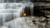 Di balik air terjun kecil di Chestnut Ridge Park, ada api yang menyala. Secara alami ada gas metana yang menyeruak kepermukaan, dan kabarnya ada seorang traveler yang pernah menghidupkan api di sini. Api ini pun masih terus menyala (Mpmajewski/CNN)