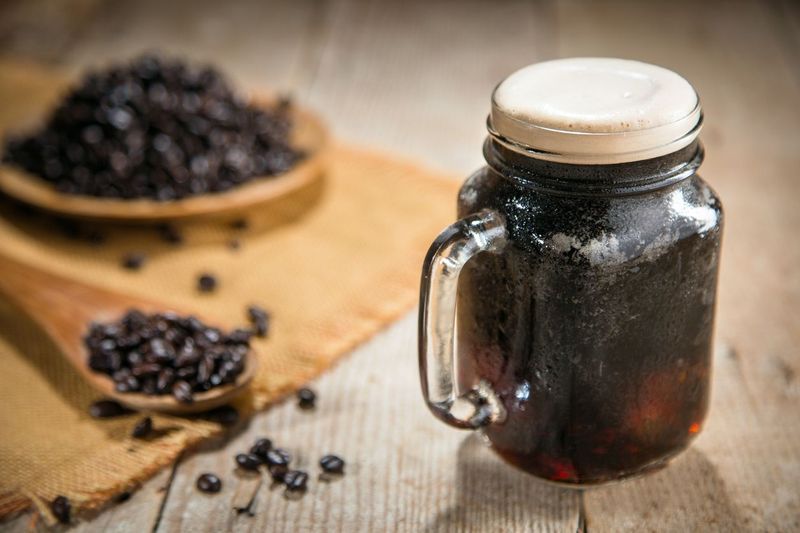 Fresh from the tap nitrous infused dark rich nitro black coffee in a glass jar java creamy beautiful froth foam head lifestyle decor with roasted beans on a rustic reclaimed wood wooden table background