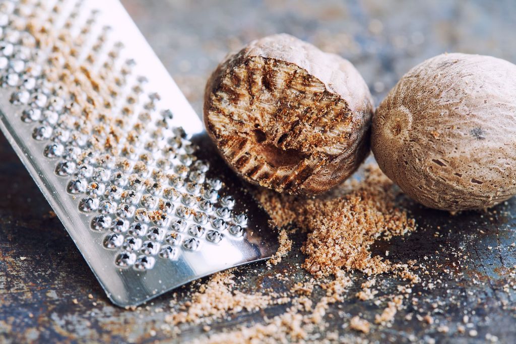 Nutmeg grater macro view. Kitchen still life photo close-up muscat nut powder. Shallow depth of field, vintage brown rusty background. Selective focus.
