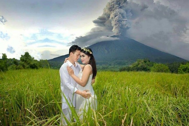 Erupsi Gunung Agung menjadi latar belakang foto pasangan yang kompak berbusana serba putih ini. Kapusdatin Humas BNPB Sutopo Purwo Nugroho‏ menulis dalam tweetnya saat mengunggah foto ini, pemotretan ekstrem ini dilakukan di Bukit Cinta yang lokasinya bukan di radius berbahaya sehingga aman untuk berfoto. Foto: Dok. Twitter Sutopo Purwo Nugroho‏