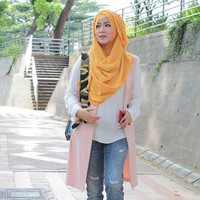 Kali ini penampilan Okie Agustina terlihat lebih kasual mengenakan celana jeans dan blouse putih. Ia menambahkan vest selutut yang membantu menutupi lekuk pinggang. Perpaduan kerudung kuning memberikan sentuhan eksentrik. Foto: Dok. Instagram @mrs.gdc13