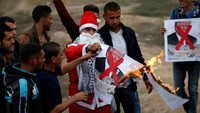 Demonstran Palestina berpakaian Santa Claus membakar poster bergambar Presiden AS, Donald Trump, ketika beraksi di perbatasan Israel kawasan timur kota Gaza. REUTERS/Mohammed Salem.