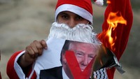 Demonstran Palestina berpakaian Santa Klaus bersama kelompoknya membakar poster bergambar Presiden AS, Donald Trump, ketika beraksi di perbatasan Israel kawasan timur kota Gaza. REUTERS/Mohammed Salem.