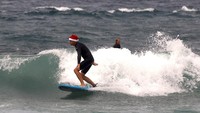 Seorang peselancar mengenakan topi khas Santa Claus di tengah terjangan ombak Pantai Bondi, Sydney, Australia. (Foto: David Gray/Reuters)