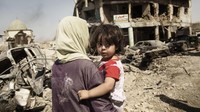 Seorang ibu tampak menggendong  seorang anak diantara puing-puing bangunan yang hancur di Mosul, Irak, pada 6 Juli 2017 lalu. Tiga tahun dilanda konflik membuat pengalaman traumatis bagi anak-anak. Luka fisik dan psikologis masih menghantui mereka hingga kini. Istimewa/UNICEF/Alessio Romenzi