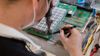 Seorang pekerja memperbaiki komponen mesin Bitcoin. Foto: Quartz