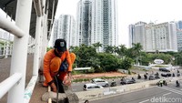 Seorang pekerja membersihkan pinggir JPO.