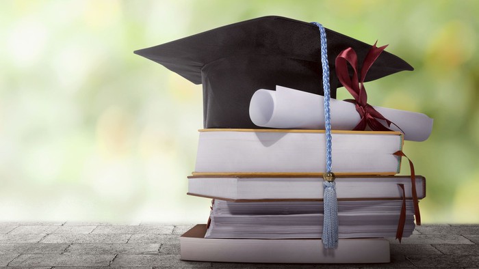 Graduation hat with degree paper on a stack of book against blurred background