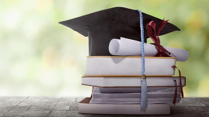 Graduation hat with degree paper on a stack of book against blurred background