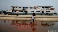 Seorang warga melintas banjir rob usai turun dari kapal di Pelabuhan Kali Adem.