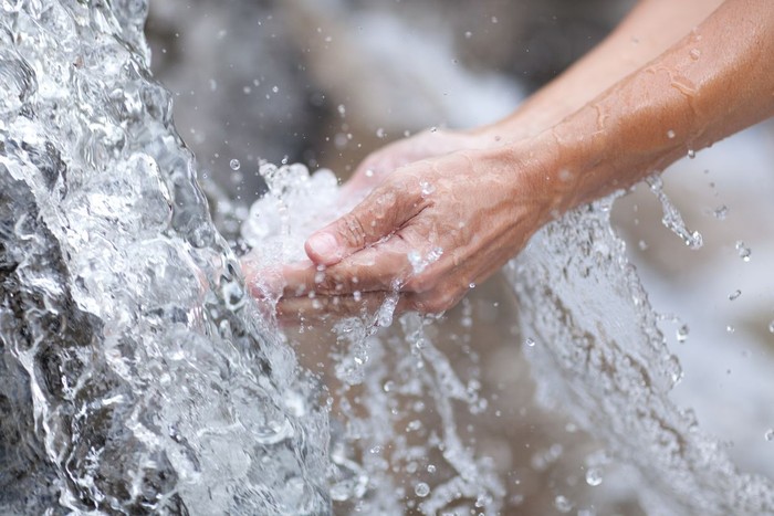 Human hand cupped to catch the fresh water from the river, reflection on water surface.