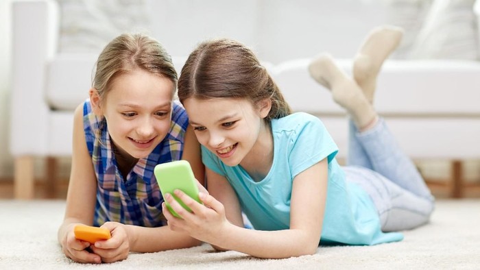 people, children, technology, friends and friendship concept - happy little girls with smartphones lying on floor at home