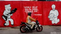 Pengendara motor melintas di sebuah mural di Penjaringan.