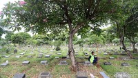 Pekerja beristirahat di bawah pohon usai membersihkan makam.