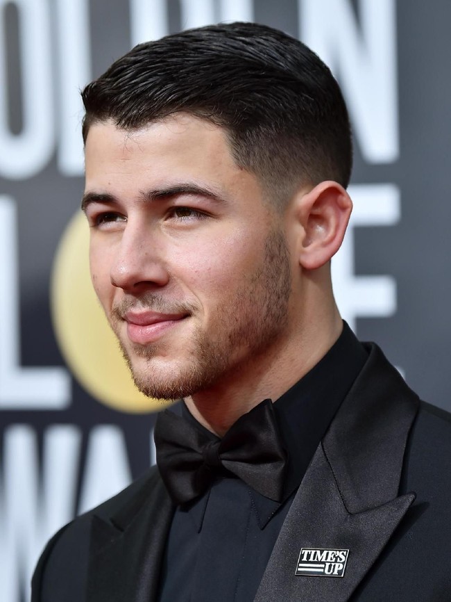Nick Jonas yang dikabarkan sedang dekat dengan Demi Moore memilih jas dengan lapel bermaterial mengkilap. Bros Time’s Up disematkannya di bagian lapel jasnya. (Foto: Getty Images)