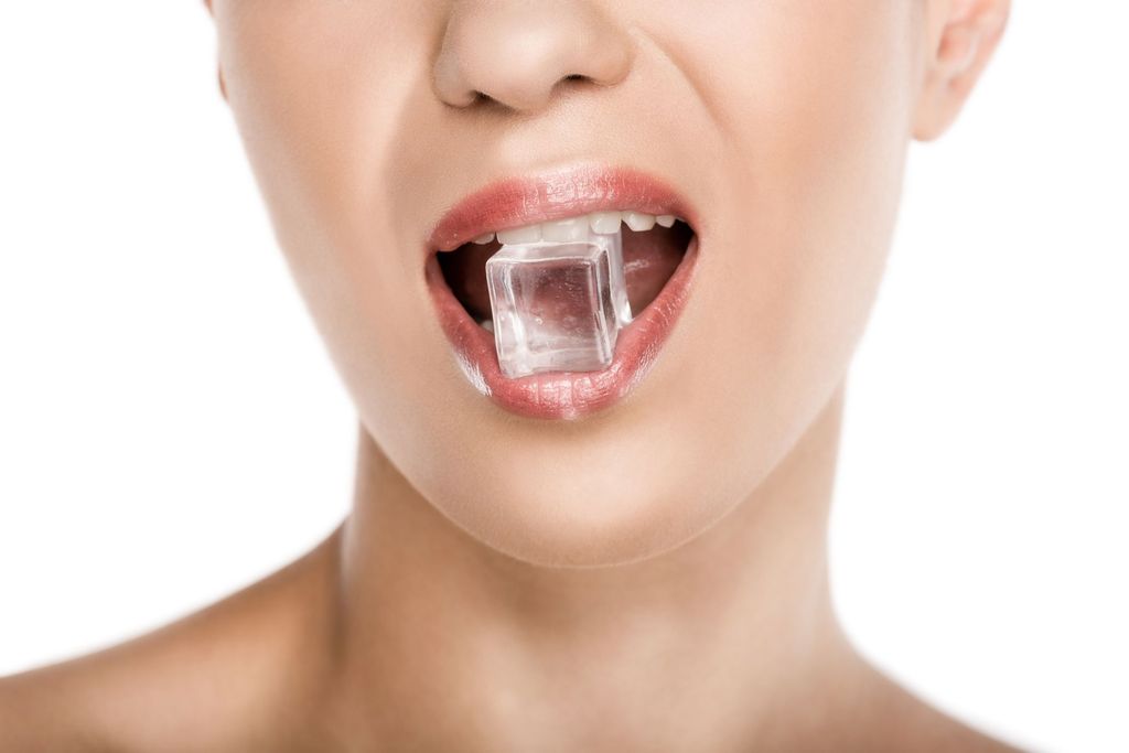 cropped view of seductive woman holding ice cube in mouth, isolated on white