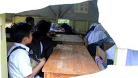 Hampir seluruh dinding fiber yang melapisi rangka kayu ruang kelas itu bolong-bolong, dari lubang itulah hujan atau angin masuk. Bila hujan, kegiatan belajar mengajar pun terhenti.