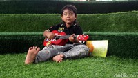 Seorang bocah terlihat asyik bermain sebuah alat musik berupa ukulele sambil bersantai.